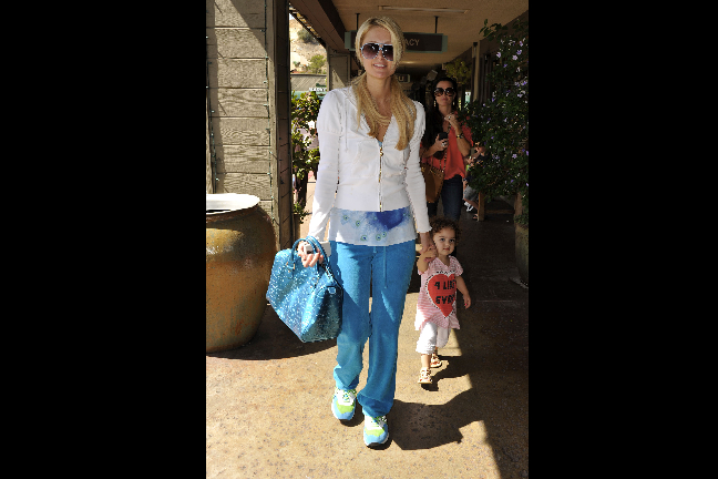 Paris Hilton i blå byxor och med lilla kusinen i handen. 